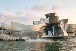 large building of curvilinear forms covered in stainless steel beside a water front